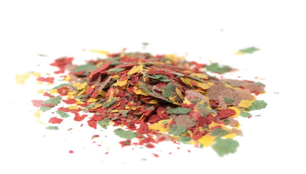 closeup of various flakes on goldfish food on white background Goldfish or Betta fish food?